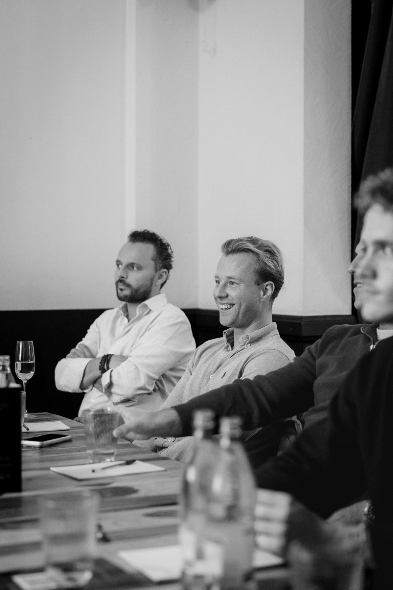 Leden volgen het gesprek aan tafel, in zwart-wit